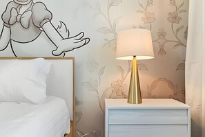 Quarto com cama, mesa de cabeceira com abajur e papel de parede floral.
