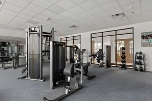 Ein Fitnessstudio mit verschiedenen Trainingsgeräten, darunter ein Squat-Gestell, eine Langhantelbank und ein Kabelzuggerät.