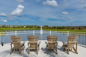 A deck with four Adirondack chairs facing a body of water, a white railing, and a clear sky. - 7 Bd / 6,5 Ba / Sleeps 18 / Solara Resort (Kissimmee)
