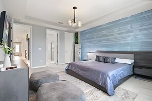 A modern bedroom with a large bed, a grey sofa, and a unique blue wall. - 7 Bd / 6,5 Ba / Sleeps 18 / Solara Resort (Kissimmee)
