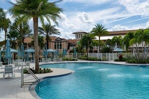 A swimming pool with lounge chairs and umbrellas, surrounded by palm trees and buildings. - 7 Bd / 6,5 Ba / Sleeps 18 / Solara Resort (Kissimmee)