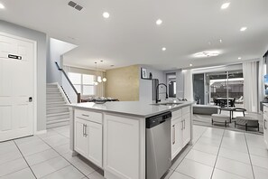 A modern kitchen with white cabinetry, a central island, and a dining area with a table and chairs. - 7 Bd / 6,5 Ba / Sleeps 18 / Solara Resort (Kissimmee)
