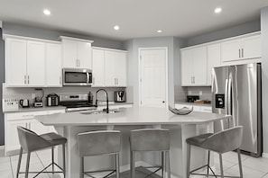 A modern kitchen with white cabinetry, a central island with bar stools, stainless steel appliances, and recessed ceiling lighting. - 7 Bd / 6,5 Ba / Sleeps 18 / Solara Resort (Kissimmee)