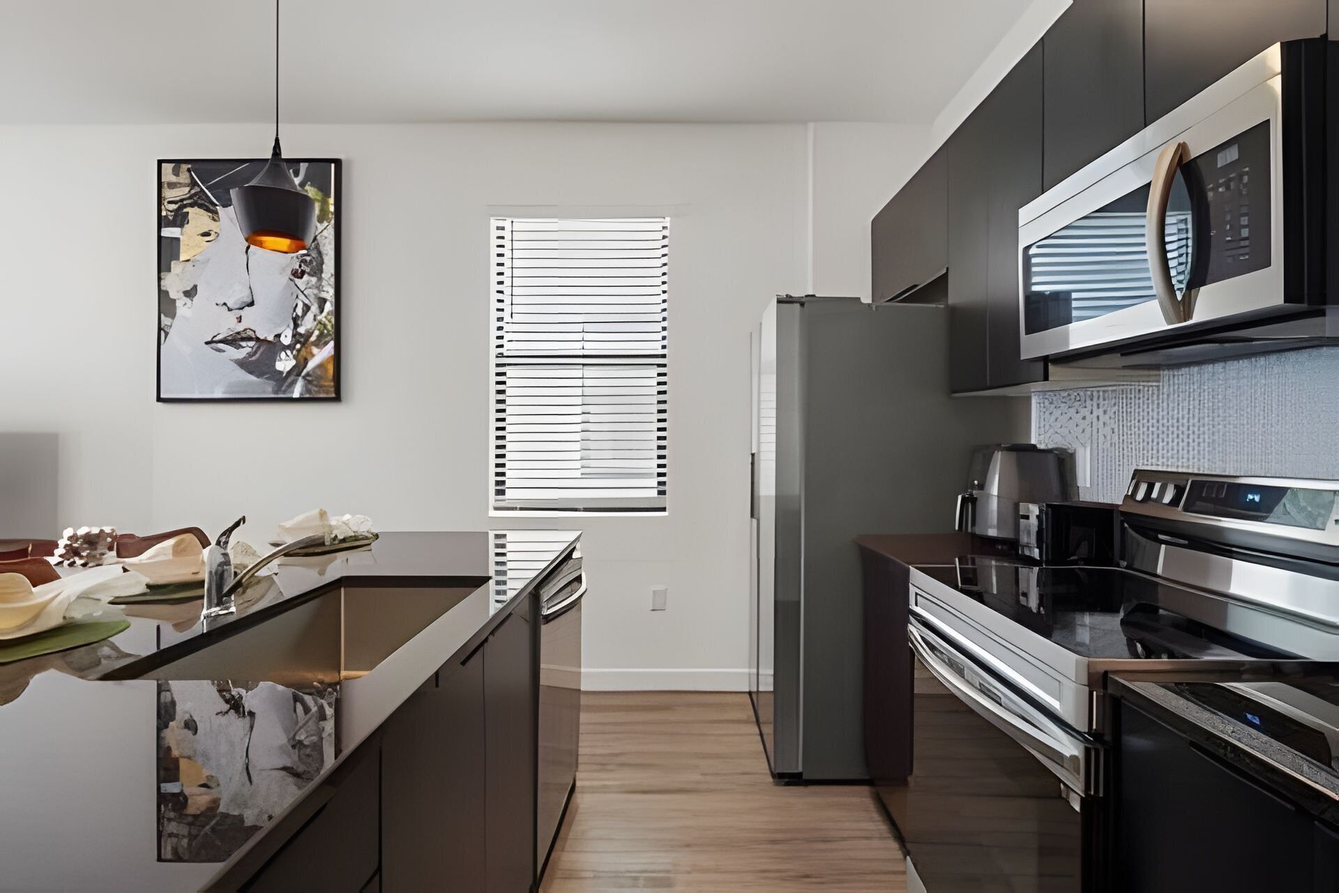 A modern kitchen with a central island, stainless steel appliances, and a large window with blinds.