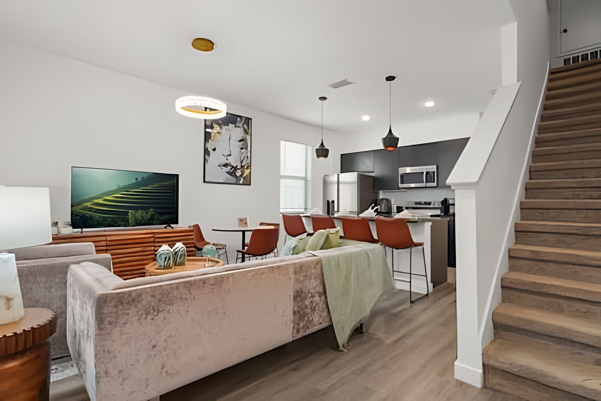 A modern living room with a sofa, a flat-screen TV, and a dining area with chairs and a table.