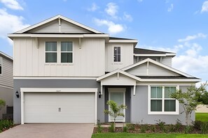 A two-story residential building with a garage, a front door, and a small front yard with a tree.