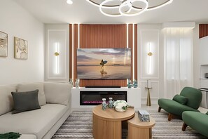 A modern living room with a large flat-screen TV mounted on a wooden panel wall, a beige sofa, a green armchair, and a round wooden coffee table. - 8 Bd / 6 Ba / Sleeps 23 / Windsor Cay Resort (Clermont)