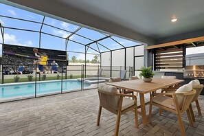 A modern outdoor patio with a pool, a dining area with wooden furniture, and a view of a mural. - 8 Bd / 6 Ba / Sleeps 23 / Windsor Cay Resort (Clermont)
