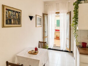 Ein Essbereich mit einem Tisch für zwei Personen, einem Gemälde an der Wand und Blick ins Freie durch eine offene Tür.