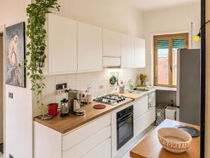 A modern kitchen with white cabinets, a stove, and a sink. - Terrazza di Jo (Roma)