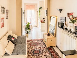 Ein modernes Wohnzimmer mit Sofa, Couchtisch, Teppich, Spiegel und einem Küchenbereich im Hintergrund.
