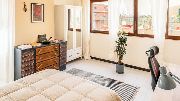 A bedroom with a bed, dresser, desk, potted plant, and a window with curtains. - Terrazza di Jo (Roma)