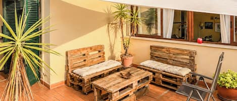 A patio with wooden furniture, a white shade sail, potted plants, and a tiled floor.