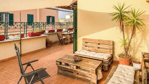 A terrace with a wooden bench, a table, and chairs. There are potted plants and a large tree. - Terrazza di Jo (Roma)