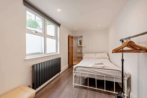 A bedroom with a bed, a radiator, a window, and a wooden hanger rack. - Host & Stay | Clarendon Violet (Brighton and Hove)