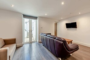 A modern living room with a sofa, a reclining chair, a flat-screen TV mounted on the wall, and a sliding glass door leading to an outdoor area. - Host & Stay | Clarendon Violet (Brighton and Hove)
