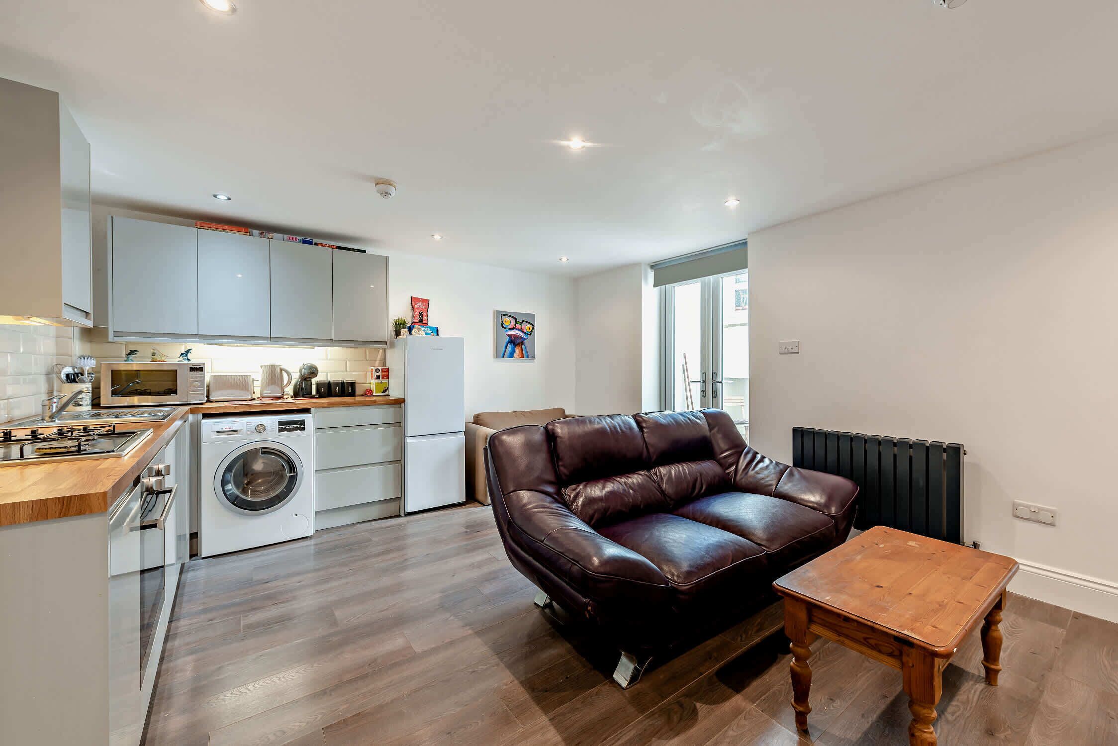 A compact living space with a kitchenette, a sofa, and a small wooden table.