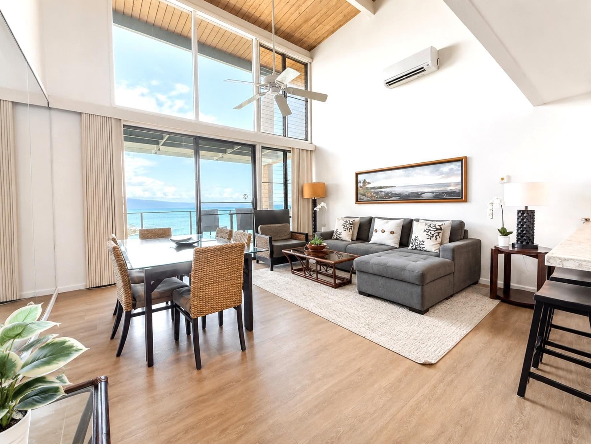 A spacious living area with a balcony overlooking the sea, a dining table with chairs, a sofa, and a coffee table.