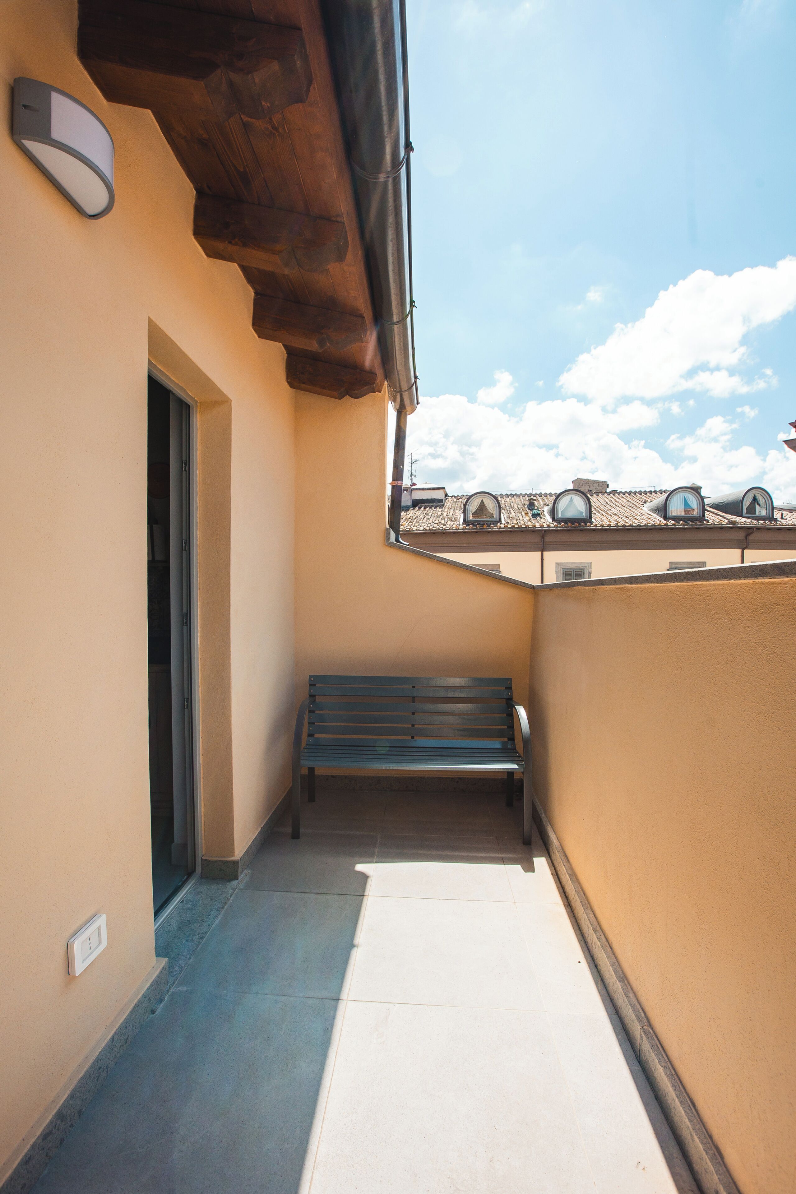 Ein schmaler Balkon mit einer Bank, einer Tür und einer Wandleuchte.