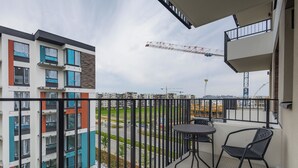 Un balcón con mesa y sillas, con vistas a una zona de construcción con grúas y edificios.