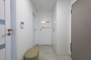 A narrow hallway with a bench, doors, and a light fixture on the wall. - Czluchowska Apartament (Warszawa)