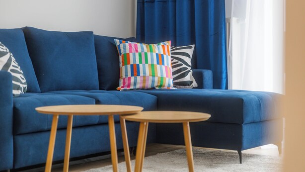 Una sala de estar moderna con un sofá azul, dos mesitas de madera redondas y almohadones coloridos.