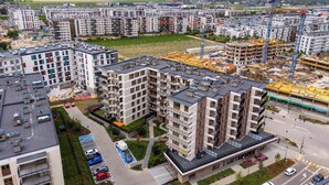Un edificio residencial de gran altura con varios balcones, un estacionamiento y una obra en construcción al fondo.