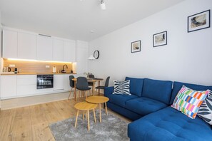 A modern living space with a kitchen, dining area, and a blue sofa with colorful pillows. - Czluchowska Apartament (Warszawa)