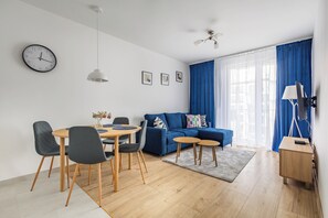 Ett modernt vardagsrum med en matplats, en blå soffa, ett matbord i trä med stolar, en takfläkt och en klocka på väggen.