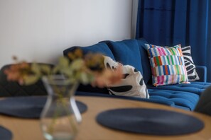 Ett modernt vardagsrum med en blå soffa, en färgglad randig kudde och en vas med blommor.