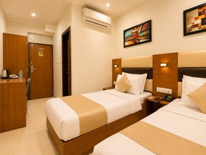 Een hotelkamer met twee bedden, een houten kledingkast, een bureau met waterkoker en een airconditioning.