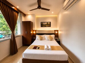 Een hotelkamer met een bed, een kledingkast, een plafondventilator, een schilderij en een raam met gordijnen.