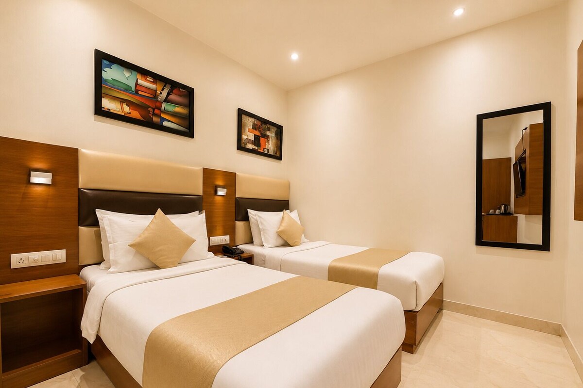 Een hotelkamer met twee bedden, een houten hoofdeinde, een nachtkastje en twee ingelijste kunstwerken, plus een spiegel bevestigd aan de muur.
