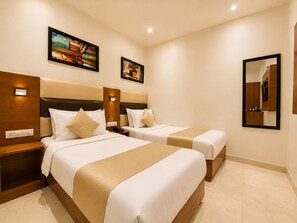 Een hotelkamer met twee bedden, een houten hoofdeinde, een nachtkastje en twee ingelijste kunstwerken, plus een spiegel bevestigd aan de muur.