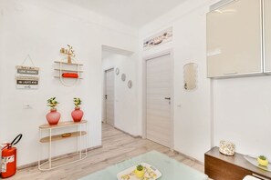 Un intérieur moderne avec un couloir menant à une porte, une petite table ornée de vases et un extincteur.