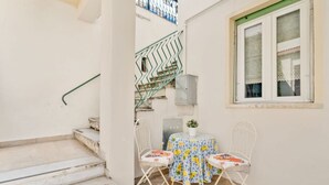 Un piccolo spazio all'aperto con tavolo e due sedie, una scala e una finestra con tenda.