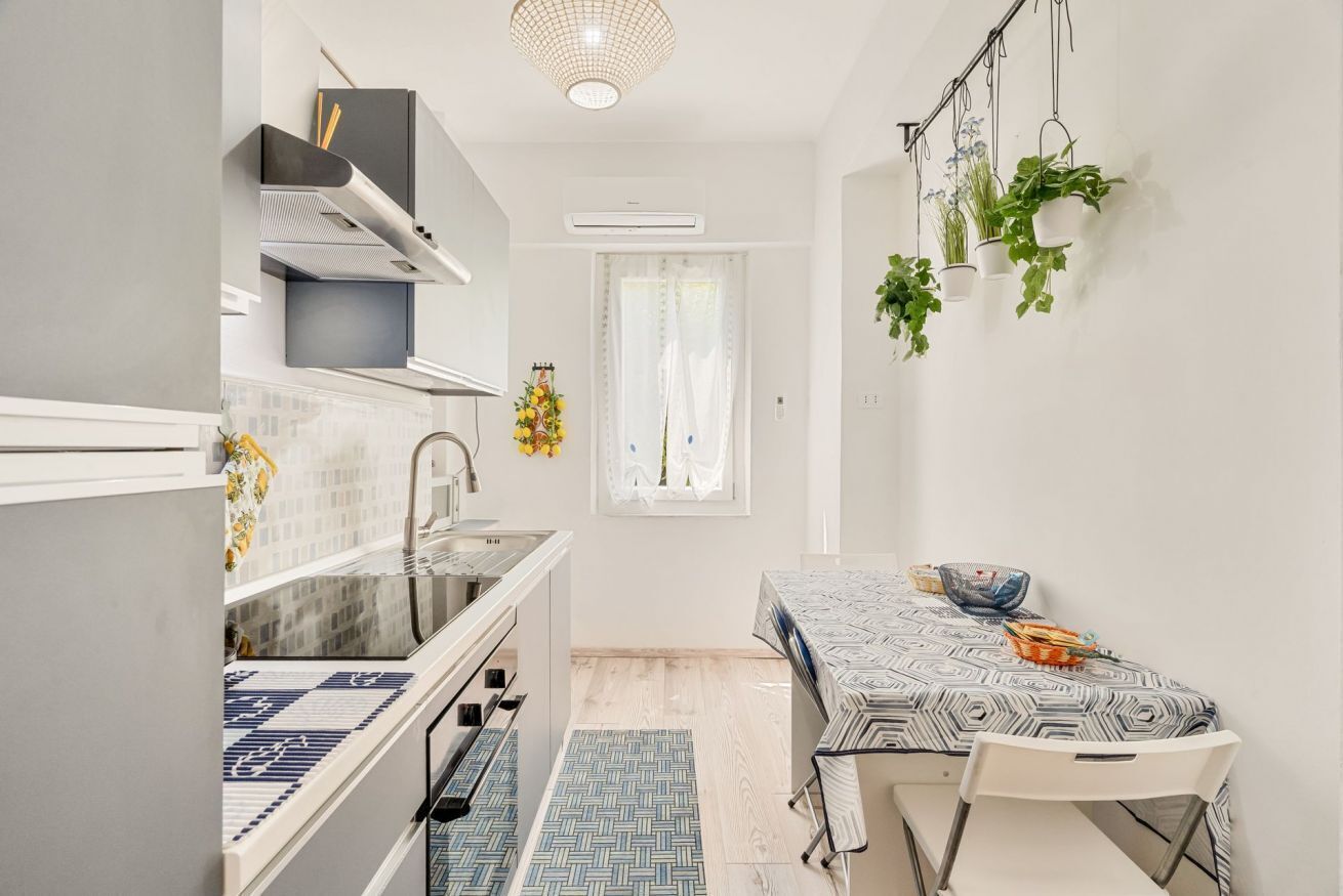A compact kitchen with a dining area, featuring a built-in oven, a sink, and a window with curtains.