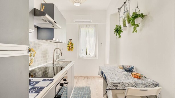 Una cucina compatta con zona pranzo, dotata di forno a incasso, lavello e finestra con tende.