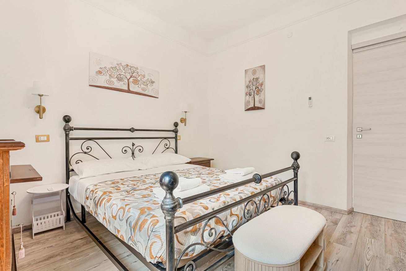 Een slaapkamer met een metalen bed, een nachtkastje, een stoel en een wandlamp.