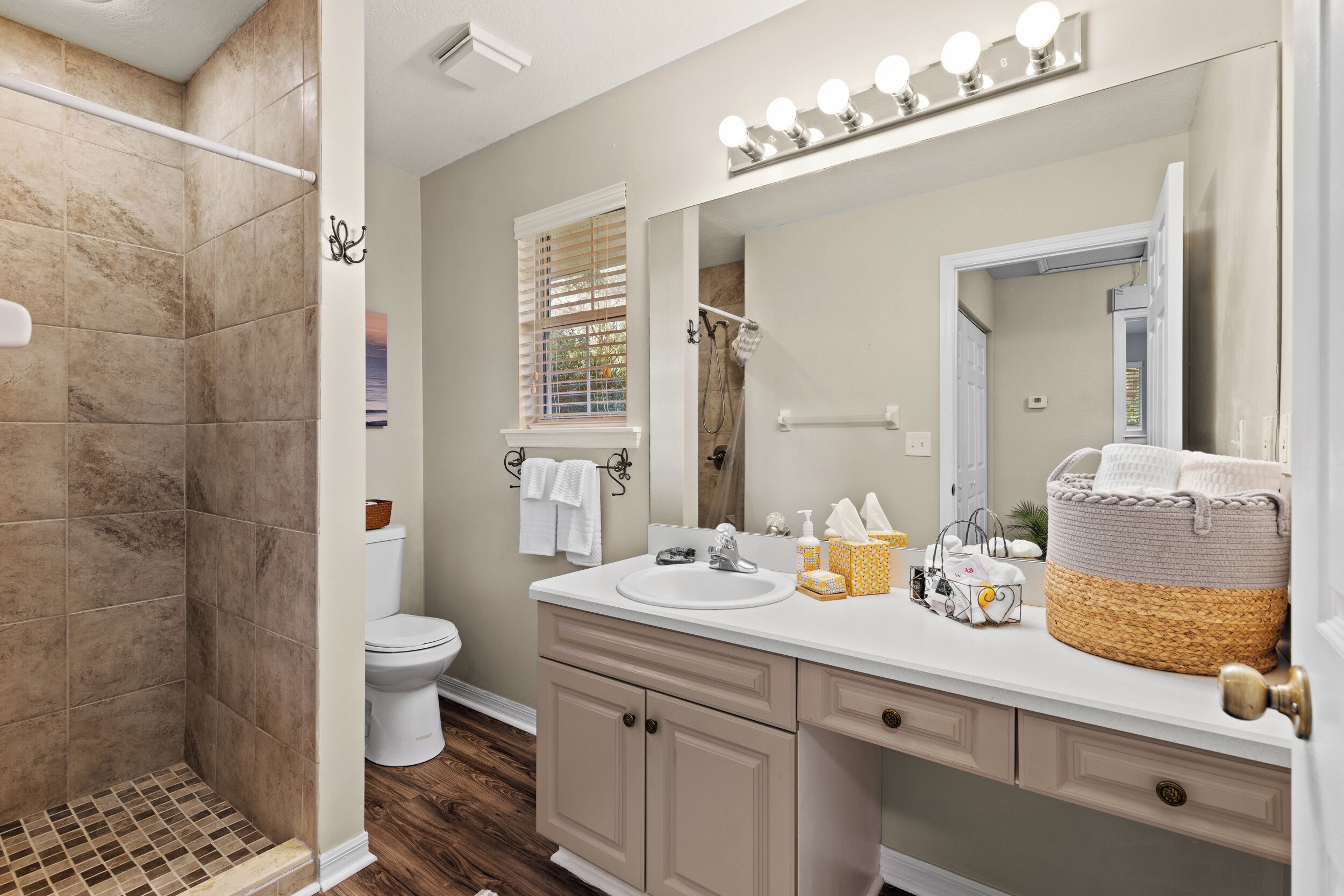 A bathroom with a shower, toilet, vanity, and a large mirror with lights.