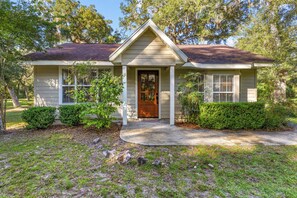 A single-story house with a front porch, a wooden door, and a small front yard with a lawn and shrubs.