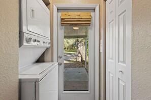 A laundry room with a washer and dryer, a wooden door, and a view of a tree-lined driveway. - Private1-bedroom cottage on “Swamp Magic Farm” close to Gainesville (Micanopy)