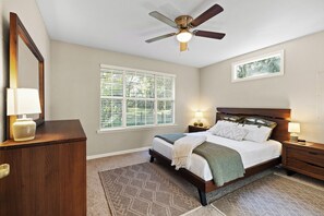 A bedroom with a bed, bedside tables, a ceiling fan, a window with blinds, and a mirror.