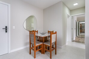 Uma área de refeições com uma mesa redonda e quatro cadeiras, um espelho grande na parede e uma porta que dá para outro quarto.