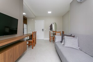 Uma sala de estar moderna com televisão de tela plana, móveis de madeira, um sofá cinza e uma área de jantar com cadeiras e mesa.