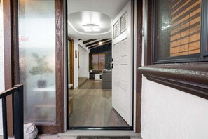 Un passadís que condueix a una zona d'estar amb una paret de pedra, una porta amb panells decoratius i un sostre amb il·luminació empotrada.