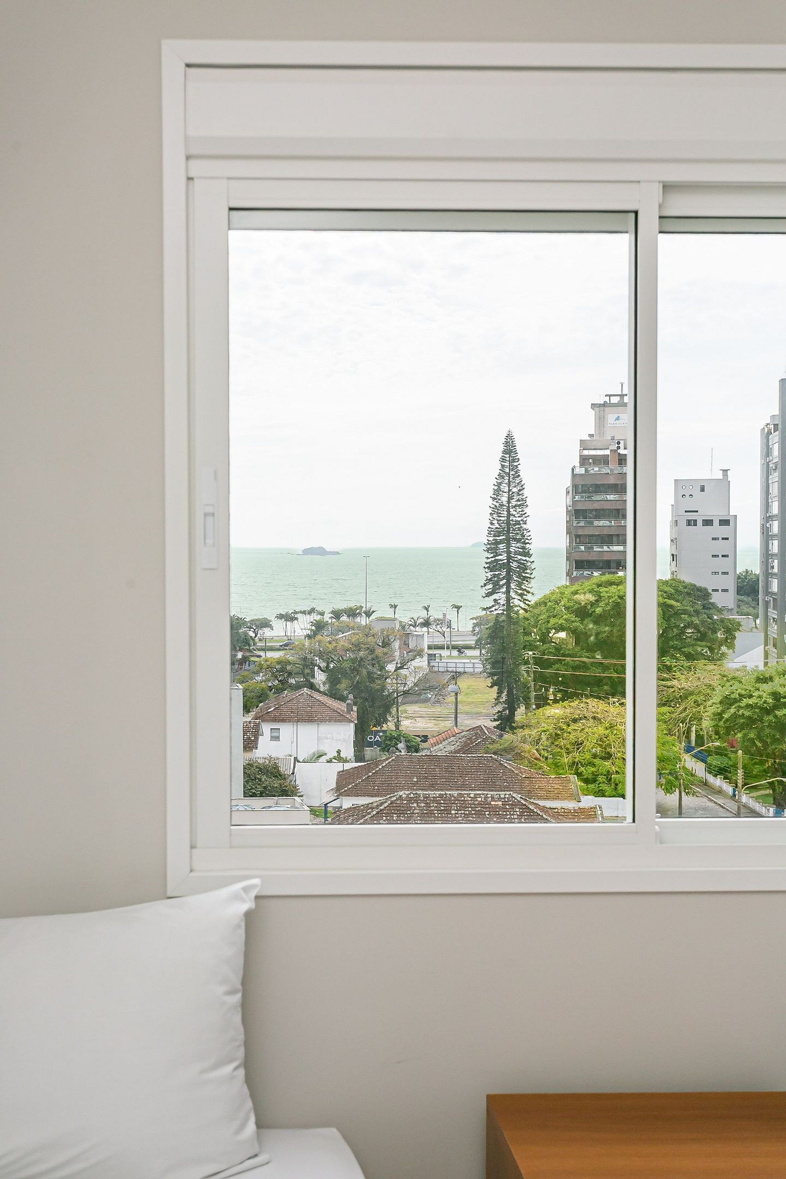 Quarto com uma grande janela com vista para a área costeira, incluindo edifícios e um corpo de água.