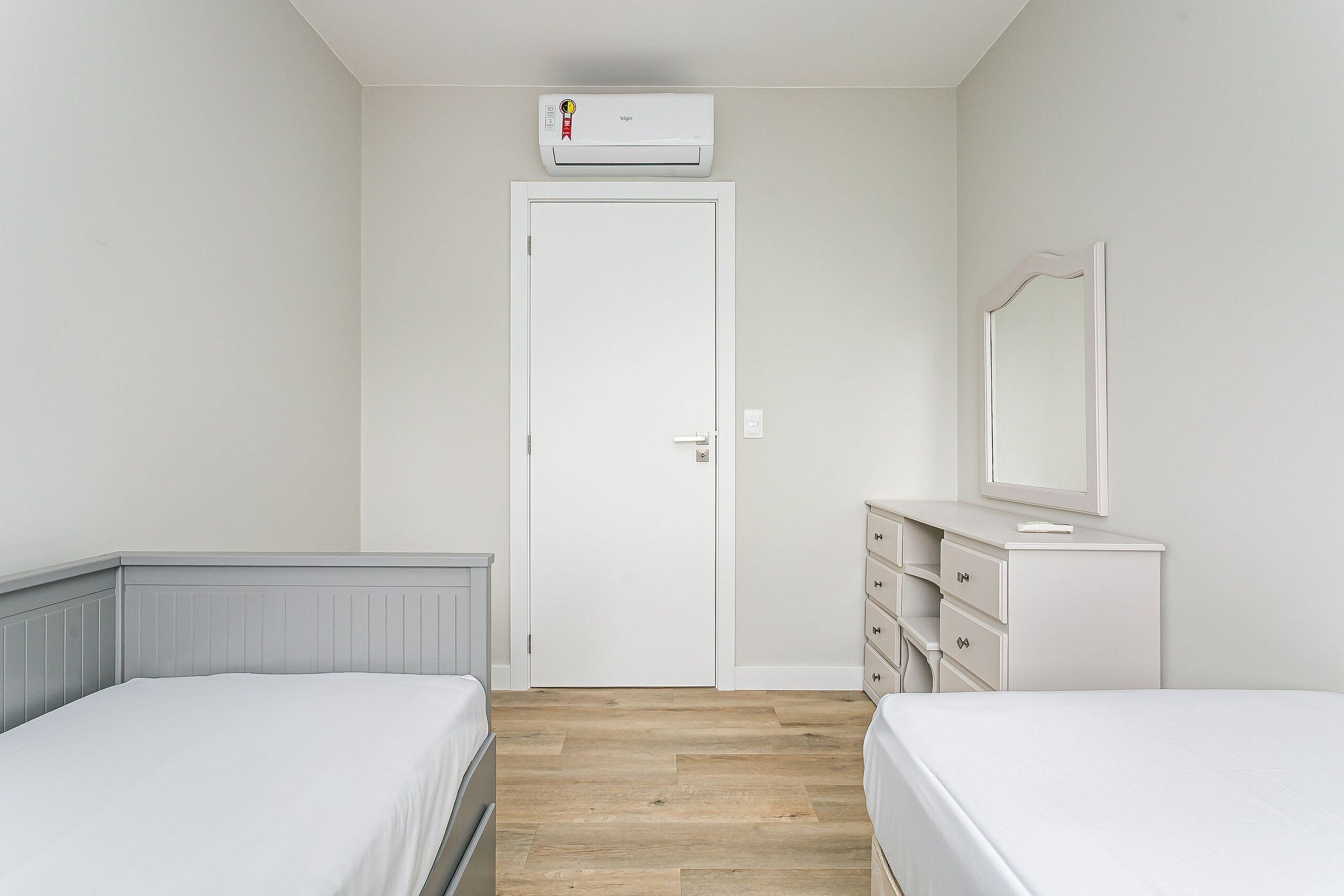 A bedroom with two beds, a dresser, a mirror, and an air conditioning unit.