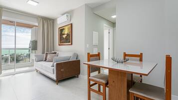 Una sala de estar moderna con un sofá, una mesa de comedor con sillas, un cuadro en la pared y vistas al exterior a través de un ventanal.