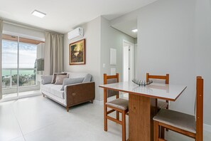 Una sala de estar moderna con un sofá, una mesa de comedor con sillas, un cuadro en la pared y vistas al exterior a través de un ventanal.
